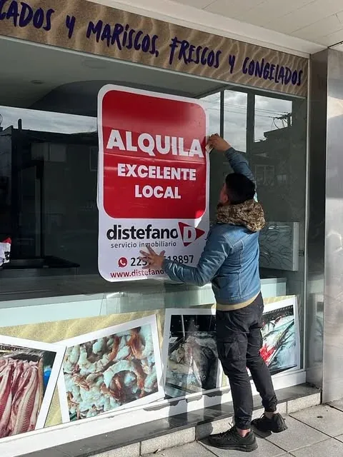 Instalación de un cartel inmobiliario rojo y blanco sobre una vidriera